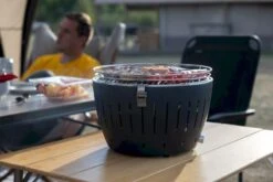 LotusGrill XL Hybrid Houtskoolbarbecue - Rood -Buitenwinkel lotusgrill in gebruik met toppy shirtje 2